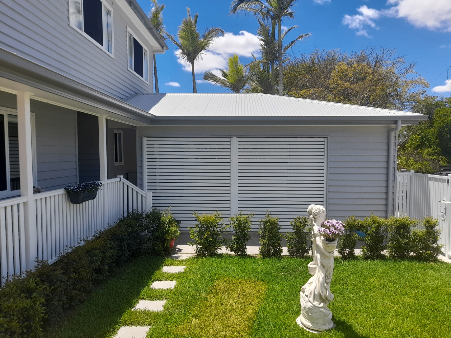 White aluminium louvre privacy screens enclosing the side of a weatherboard home with landscaped front yard - Gateflex, Caboolture