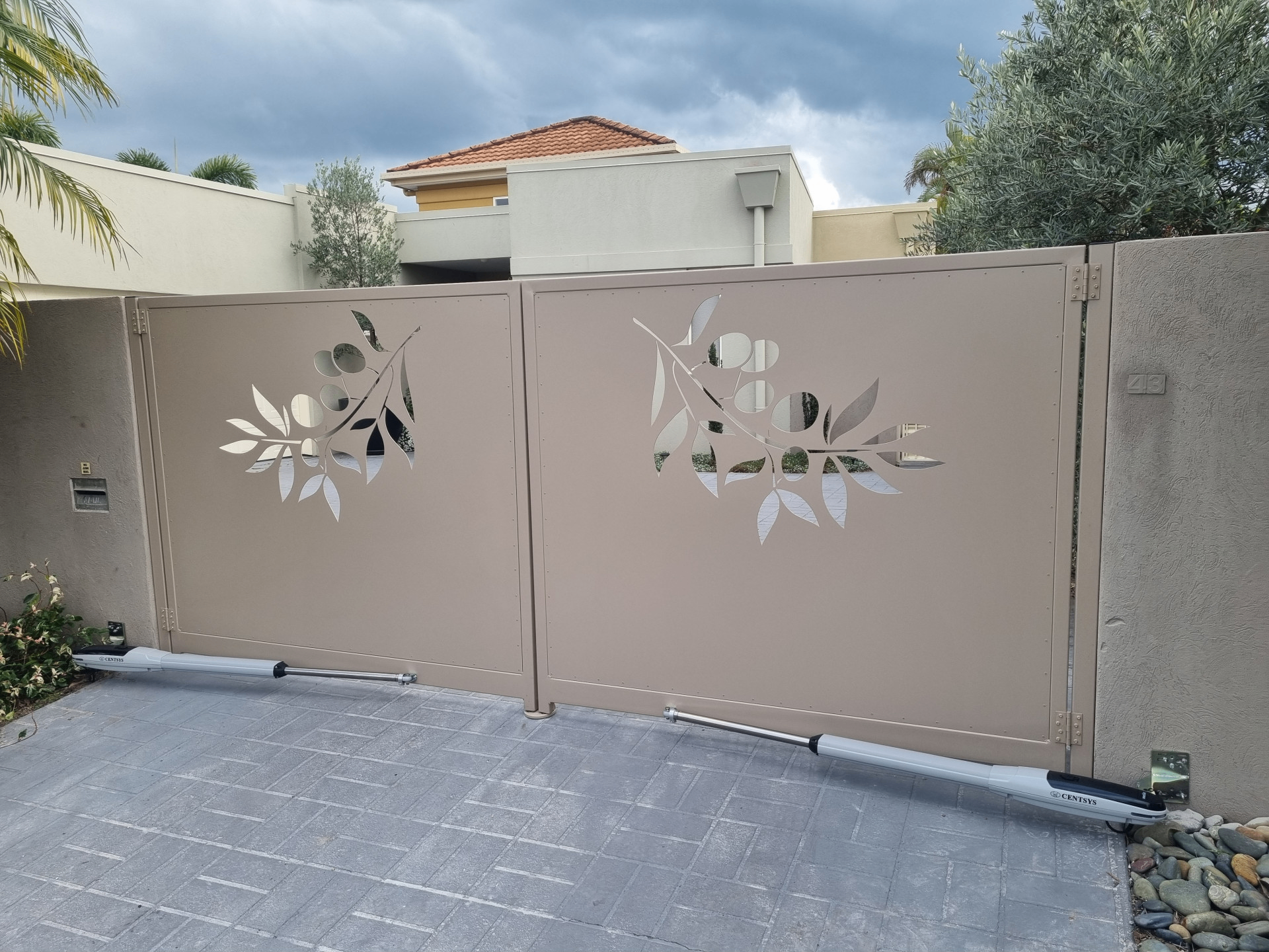 Beige aluminium double swing driveway gate with laser-cut olive branch design and automation arms - Gateflex, Caboolture